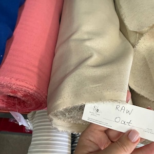 以下が含まれることがあります： RAW Oatと書かれたラベルが付いたライトベージュの生地のロール。コーラルピンクの生地のロールと青い生地のロールの隣にあります。ラベルにはSECRETSPARKFABRICS.COMおよびSECRETSPARKFABRICS.ETSY.COMのテキストと、SSの文字が入ったロゴが含まれています。