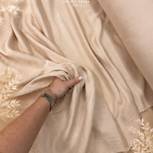 May include: A bolt of beige fabric with a soft, crinkled texture. The material is draped loosely, showing raw, frayed edges. A logo featuring the text SECRET SPARK fabrics is visible at the top, and copyright text appears at the bottom.