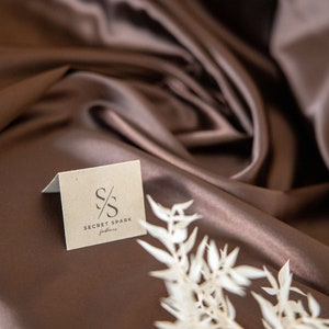 May include: A brown fabric backdrop with a small, white card featuring the logo "S/S SECRET SPARK fabrics" in black text.