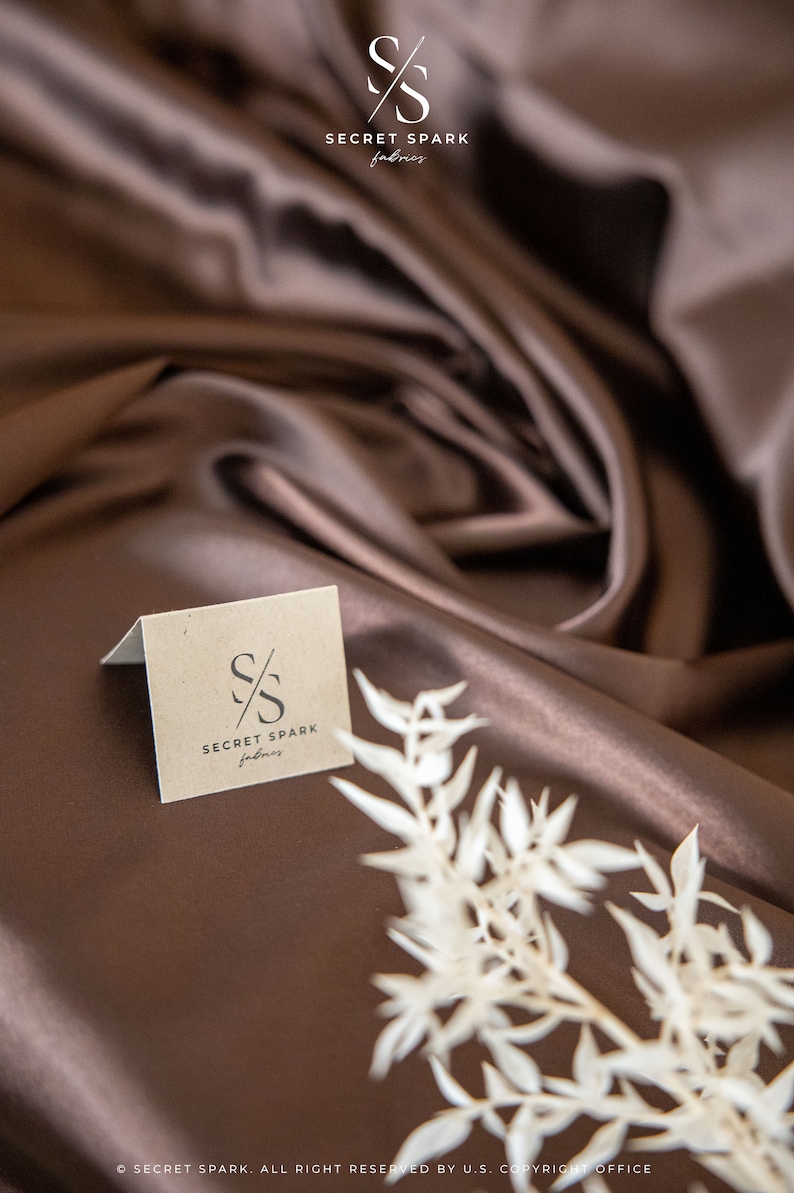 May include: A brown fabric backdrop with a small, white card featuring the logo "S/S SECRET SPARK fabrics" in black text.
