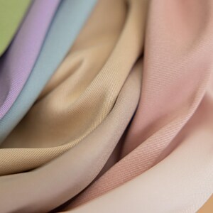 May include: Close-up of a selection of fabric swatches in shades of beige, pink, and blue. The fabric is smooth and has a subtle texture. The text "SECRET SPARK fabrics" is visible in the top centre of the image.