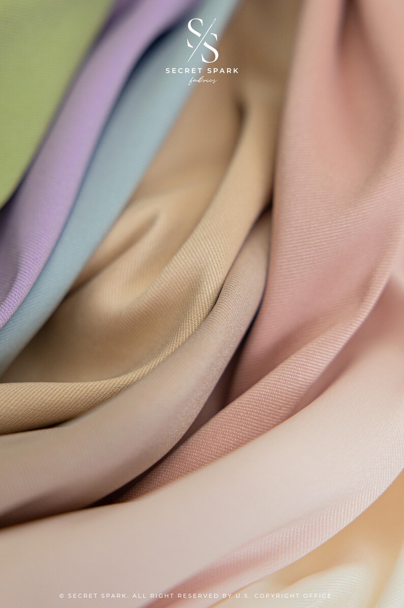 May include: Close-up of a selection of fabric swatches in shades of beige, pink, and blue. The fabric is smooth and has a subtle texture. The text "SECRET SPARK fabrics" is visible in the top centre of the image.