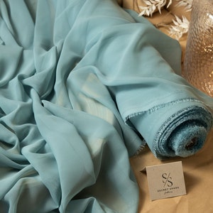 May include: A roll of light blue chiffon fabric with a frayed edge. The fabric is folded and rolled up, and the label "SECRET SPARK fabrics" is visible.