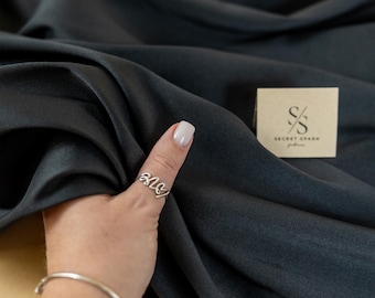 Tejido de sarga de satén mikado negro mate con textura granular de élite, caída estructurada y peso considerable para vestidos.