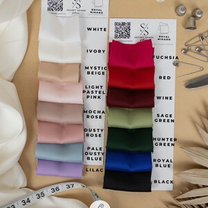 May include: A swatch card displaying 12 different colours of stretch satin fabric called "Royal Mikado". The fabric is described as having a luxurious high-density texture with an elite granular texture. The fabric is 92% polyester and 8% spandex. The colours are white, ivory, mystic beige, light pastel pink, mocha rose, dusty rose, pale dusty blue, lilac, fuchsia, red, wine, and sage green.