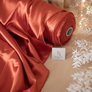 May include: A roll of rust-colored satin fabric with a white label that says "Secret Spark Fabrics".