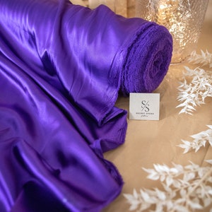 Pu&ograve; includere: Un rotolo di tessuto di raso viola con un'etichetta che dice "Secret Spark Fabrics".