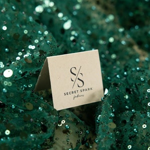 May include: A brown card with the text "SECRET SPARK fabrics" and a stylized "SS" logo on a green sequined fabric background.