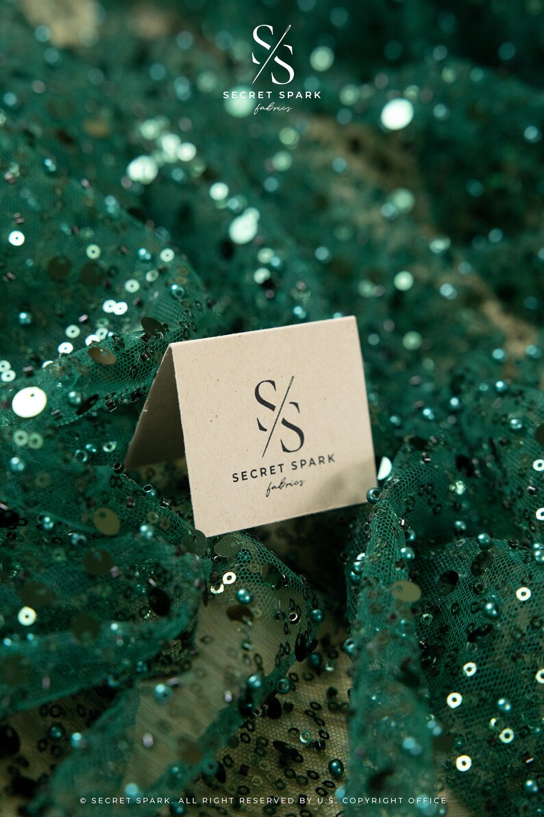 May include: A brown card with the text "SECRET SPARK fabrics" and a stylized "SS" logo on a green sequined fabric background.