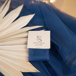 May include: A close-up of a brown card with the text "SECRET SPARK snatches" and a logo of two overlapping "S" letters. The card is on top of a blue fabric with a white palm leaf.