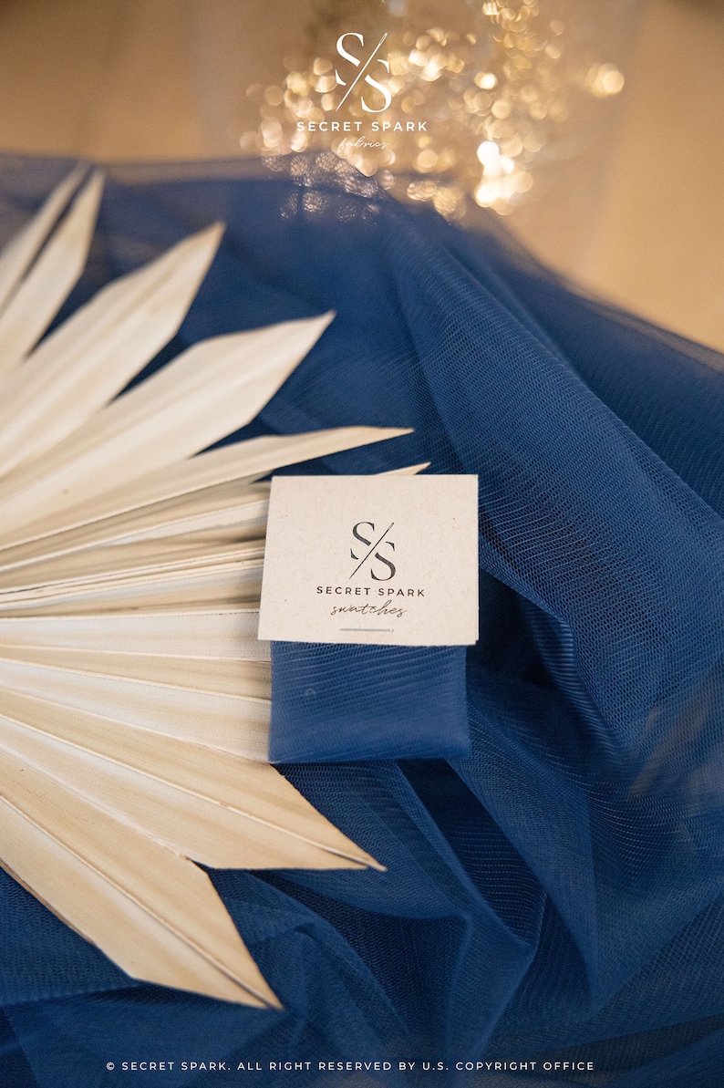May include: A close-up of a brown card with the text "SECRET SPARK snatches" and a logo of two overlapping "S" letters. The card is on top of a blue fabric with a white palm leaf.