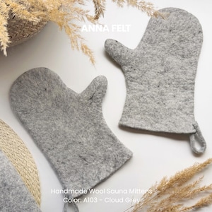 May include: Two handmade cloud gray wool sauna mittens. The mittens are made of a soft, felted material. The text "ANNA FELT" is visible at the top of the image. The text "Handmade Wool Sauna Mittens Color: A103 - Cloud Grey" is visible at the bottom.