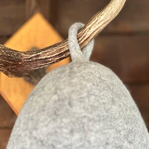 K&ouml;nnte beinhalten: Ein grauer Filzhut, der an einem Holz-Hirschhornhaken h&auml;ngt. Der Hut ist weich und hat eine abgerundete Form.