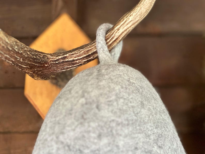 K&ouml;nnte beinhalten: Ein grauer Filzhut, der an einem Holz-Hirschhornhaken h&auml;ngt. Der Hut ist weich und hat eine abgerundete Form.