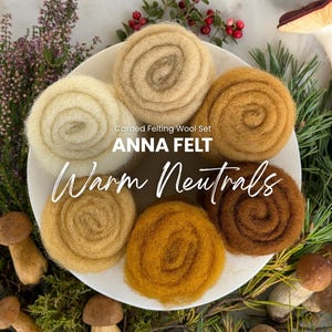 Op de afbeelding: Een set van zes opgerolde strengen gekaarde viltwol in diverse tinten crème, beige, goud en bruin op een wit bord. De tekst op het bord luidt Carded Felting Wool Set ANNA FELT Warm Neutrals.