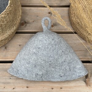 K&ouml;nnte beinhalten: Ein grauer Filzhut mit einem Schlaufe. Der Hut liegt auf einer Holzoberfl&auml;che.