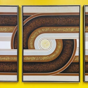May include: Triptych abstract art piece with a retro design. The artwork features brown, gold, and white geometric shapes and lines. The pieces are framed in gold and mounted on a yellow background.