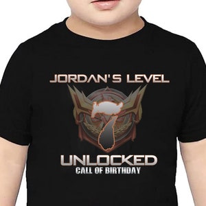May include: Black t-shirt with a gold and red graphic design. The graphic features a number 7 with a crown and the text "JORDAN'S LEVEL UNLOCKED CALL OF BIRTHDAY".