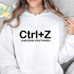 May include: White hoodie with a black graphic that says "Ctrl+Z Undoing Mistakes..."
