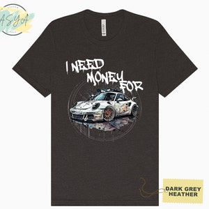 May include: Dark grey heather t-shirt featuring a white sports car graphic and the text "I NEED MONEY FOR" in white graffiti-style lettering.