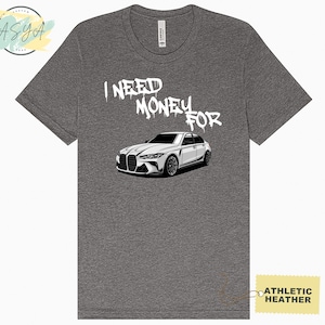 May include: A gray t-shirt with the text "I NEED MONEY FOR" in white spray paint and a white car illustration below. The t-shirt is labeled "Athletic Heather".