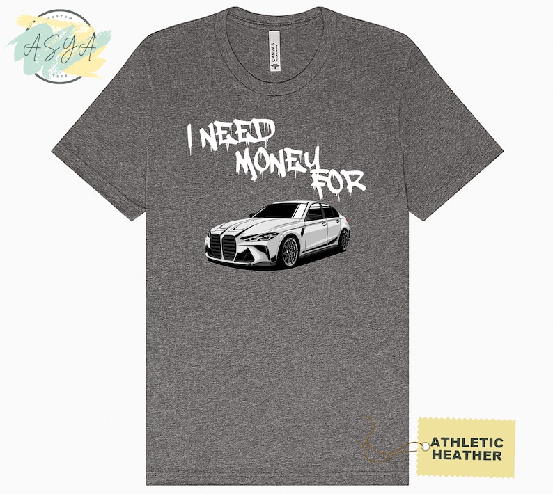 May include: A gray t-shirt with the text "I NEED MONEY FOR" in white spray paint and a white car illustration below. The t-shirt is labeled "Athletic Heather".