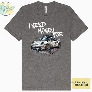 May include: Grey t-shirt featuring a white sports car graphic and the text "I NEED MONEY FOR" in white spray paint.