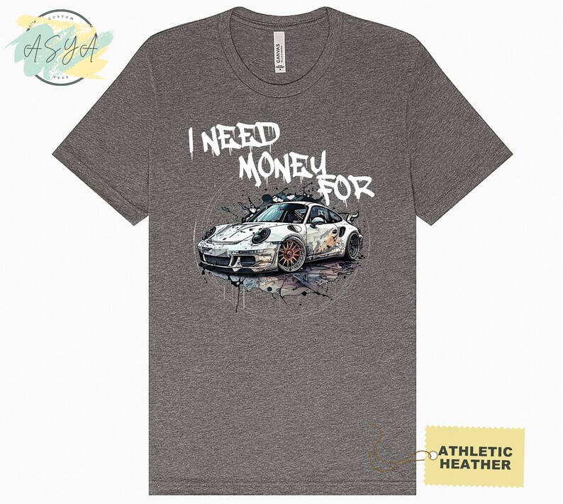 May include: Grey t-shirt featuring a white sports car graphic and the text "I NEED MONEY FOR" in white spray paint.