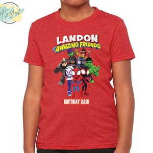 Pode incluir: Camiseta vermelha com um gr&aacute;fico de super-her&oacute;is de desenhos animados e o texto "Landon's Amazing Friends Birthday Bash".