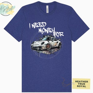 May include: A blue heather t-shirt featuring a white graphic of a sports car and the text "I NEED MONEY FOR" in white graffiti-style lettering.