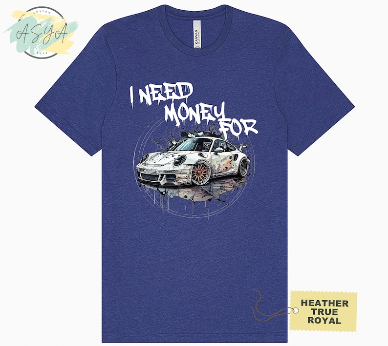 May include: A blue heather t-shirt featuring a white graphic of a sports car and the text "I NEED MONEY FOR" in white graffiti-style lettering.