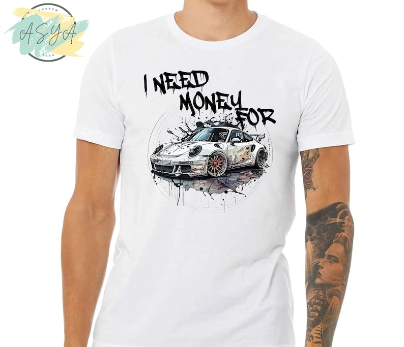 May include: White t-shirt with a black graphic print of a white sports car with the text "I NEED MONEY FOR" above it.