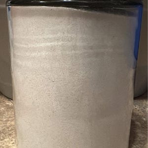 May include: A clear glass jar with a silver lid filled with white powder. The jar is sitting on a brown surface.