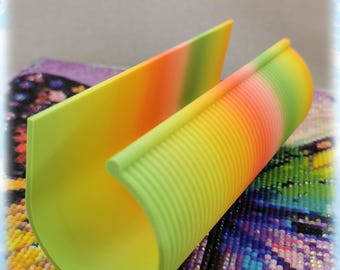 May include: A rainbow-colored silicone tool for diamond painting. The tool has a ribbed surface and a curved shape to help hold the canvas in place.
