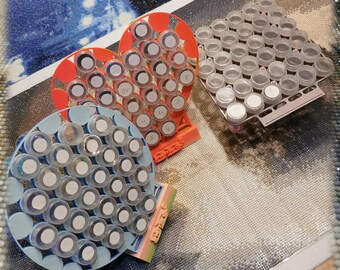 May include: Three heart-shaped organizers for diamond painting, each with rows of small containers for storing beads. The organizers are in blue, pink, and orange.