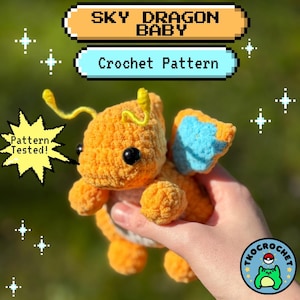 May include: An orange crocheted dragon toy with black eyes and blue wings. The text "SKY DRAGON BABY Crochet Pattern" is displayed above the dragon. The text "Pattern Tested!" is also visible. A logo with a frog is in the bottom right corner.