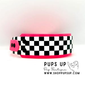 Puede incluir: Un collar para perros de color rosa intenso con un diseño de cuadros blancos y negros. El collar tiene un cierre de hebilla. El texto "PUPS UP Dog Boutique" y "WWW.SHOPPUPSUP.COM" es visible.