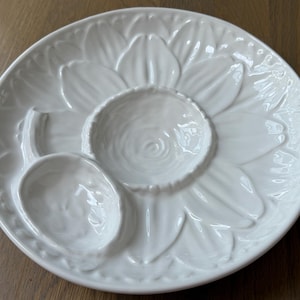 May include: White ceramic serving platter in the shape of a sunflower. The platter has a central dip bowl and two additional sections for serving. The sunflower design is embossed on the surface.