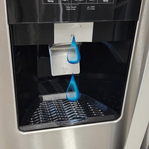 May include: A stainless steel refrigerator with a black control panel featuring buttons for freezer temperature, light, ice type, and lock. The panel also displays a filter reset message. Water is dispensing from the dispenser.