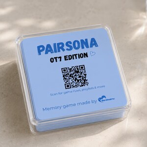 Op de afbeelding: Een vierkant doorzichtig plastic doosje met een stapel lichtblauwe kaarten. De bovenste kaart bevat de tekst PAIRSONA OT7 EDITION, een klein hartje, een zwarte QR-code, de tekst Scan for game rules, playlists & more en Memory game made by Borahearts.