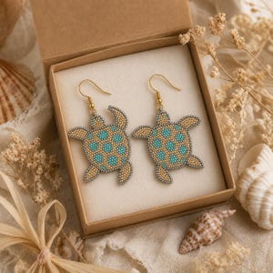 Peut inclure: Une paire de boucles d'oreilles en forme de tortue de mer, fabriquées à partir de petites perles dans des tons beige et turquoise. Les boucles d'oreilles sont dotées de crochets en métal doré et présentées dans une boîte en carton carrée.