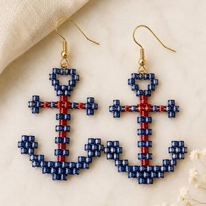 May include: A pair of dangle earrings featuring anchor-shaped charms crafted from small, cylindrical beads. The anchors are primarily dark blue with a central vertical stripe of red beads. Each earring hangs from a gold-toned metal hook.