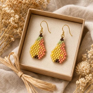 May include: A pair of pear-shaped drop earrings crafted from small, square beads in shades of yellow, light green, and soft pink. The earrings feature gold-toned metal hooks and are displayed inside a square, light brown cardboard gift box.