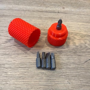 Könnte beinhalten: Ein rotes Plastiketui mit einem passenden roten Plastikschraubendreher mit schwarzer Spitze. Das Etui ist geöffnet und enthält fünf schwarze Schraubendreherbits in verschiedenen Größen.