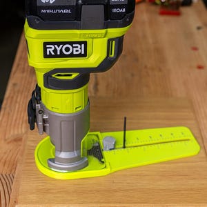 May include: A cordless RYOBI router with a lime green and black design, featuring a 18V lithium battery. The router is shown with a yellow base and a ruler, ideal for woodworking projects.