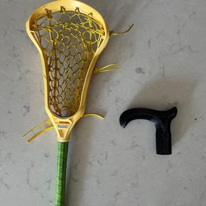 May include: A yellow lacrosse stick with a green grip and a black cane handle.