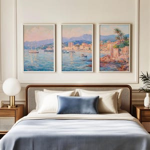 Pode incluir: Interior de quarto com uma cama com edredão azul, almofadas brancas e uma almofada azul. Acima da cama, três pinturas emolduradas de paisagens costeiras com barcos e edifícios. Uma lâmpada dourada e mesas de cabeceira de madeira completam a decoração.