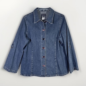 May include: A medium-wash denim jacket with a button-up front, collared neckline, and long sleeves. The jacket has a classic design with a few decorative details on the sleeves and red buttons. The brand tag is visible on the collar.