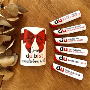 May include: A white gift box with a red bow and the text "Oma du bist wunderbar, weil" on it.  There are five white tubes with red and gold accents and the word "du" on them. Each tube has a different message on it.