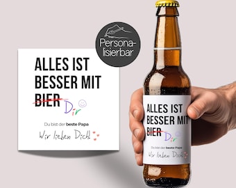 May include: A white card with black text that reads "Alles ist besser mit Bier" with the word "Bier" crossed out and the word "Dir" written in. The card also says "Du bist der beste Papa" and "Wir lieben Dich!" A brown beer bottle with a white label that reads "Alles ist besser mit Bier" with the word "Bier" crossed out and the word "Dir" written in. The label also says "Du bist der beste Papa" and "Wir lieben Dich!"